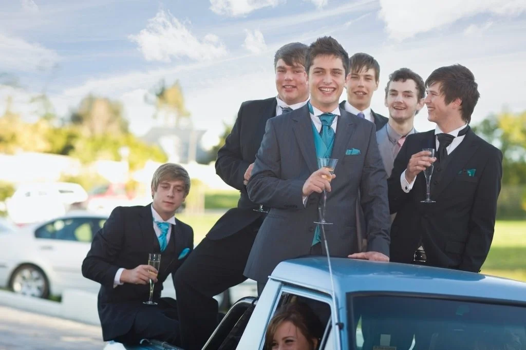 Teenage boys in suits smiling from car